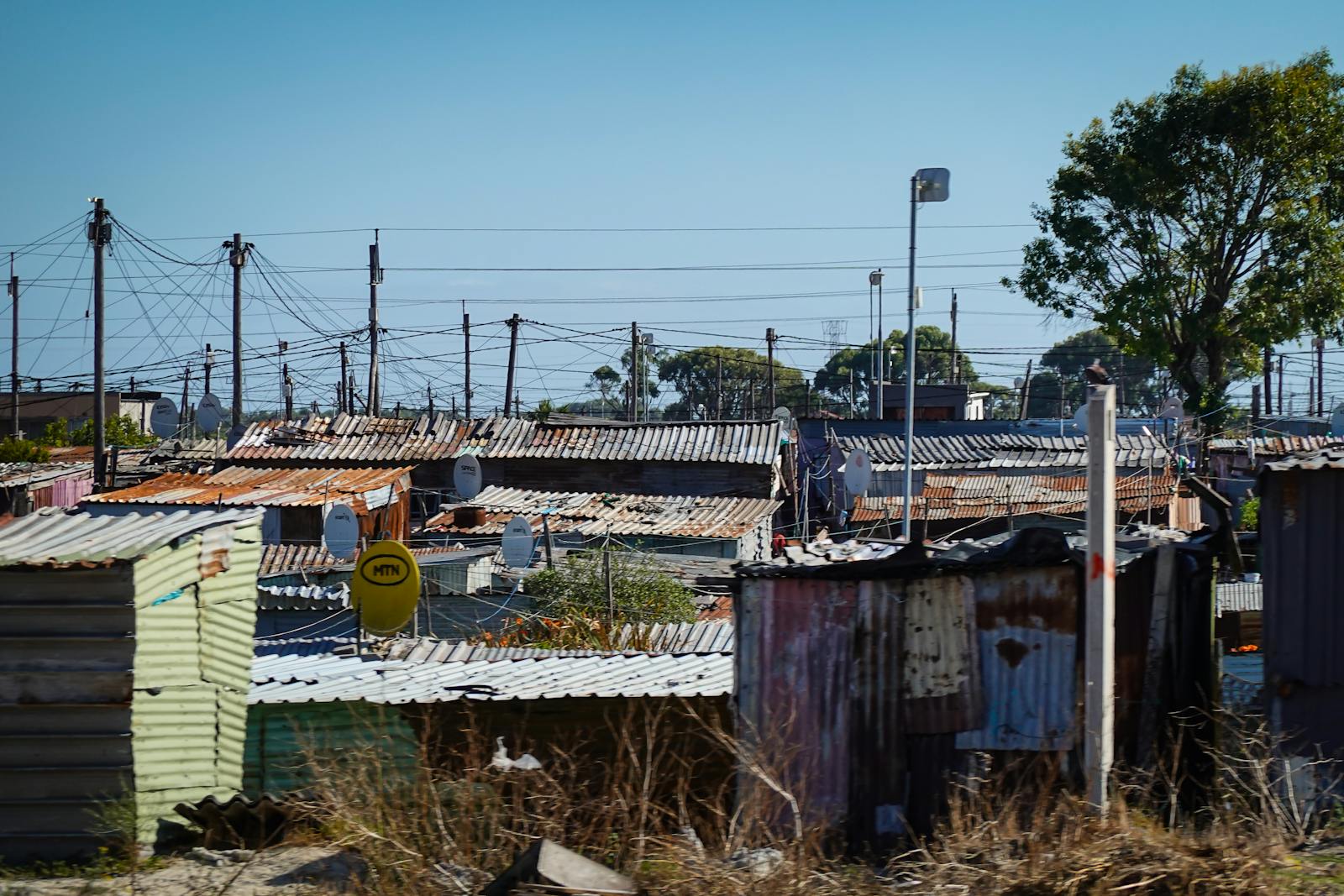 A view of an informal settlement with numerous makeshift rooftops and power lines.