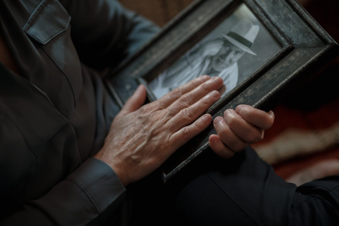 Elderly person holding and touching a framed photo of a deceased loved one in remembrance