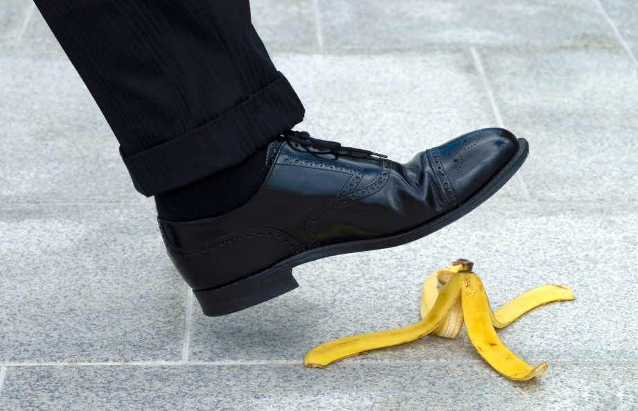 Close-up of a person about to slip on a banana peel while walking on a tiled floor